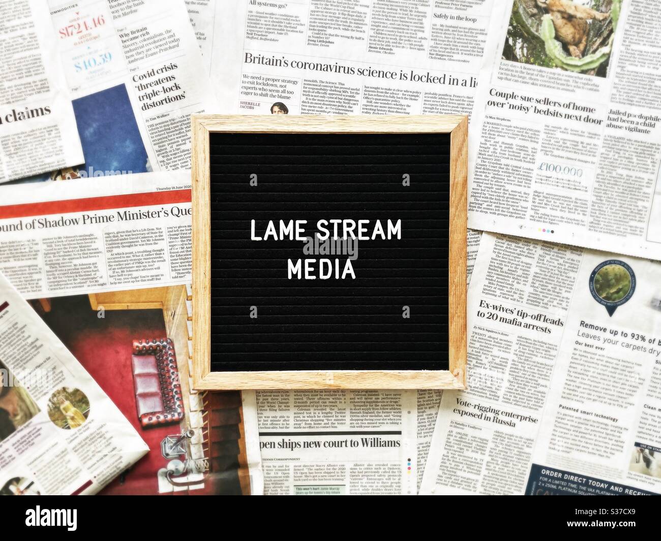 A closeup view of a black felt message board with the phrase Lame stream media, seen against a background of national newspaper pages. Headlines, tabloids, press and media concepts. Stock Photo