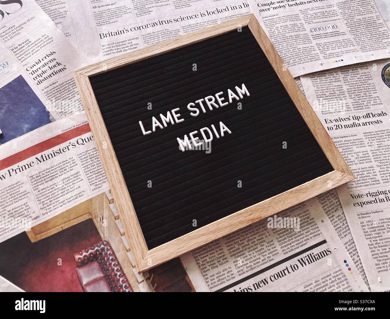 A closeup view of a black felt message board with the phrase Lame stream media, seen against a background of national newspaper pages. Headlines, tabloids, press and media concepts. Stock Photo