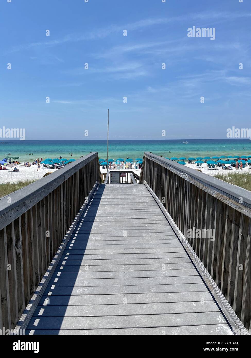 Wooden bridge leading to white sand beach with view of emerald water of the Gulf of Mexico - Smartphone Captured Stock Image
