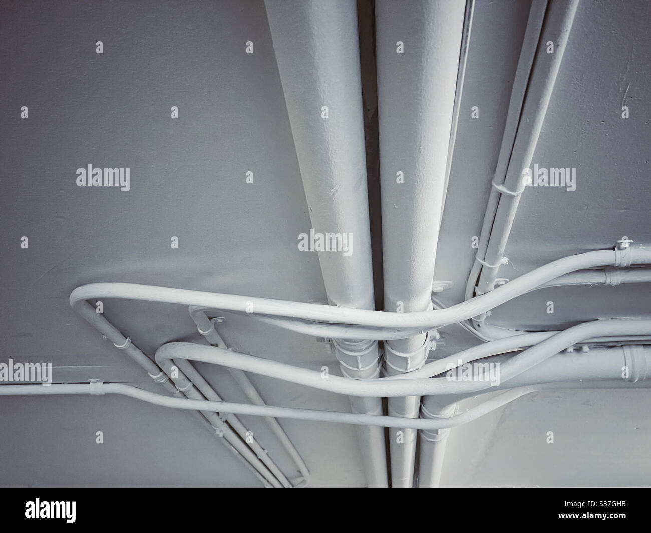 White painted water pipes crisscrossing on the ceiling of a garage - Smartphone Captured Stock Image