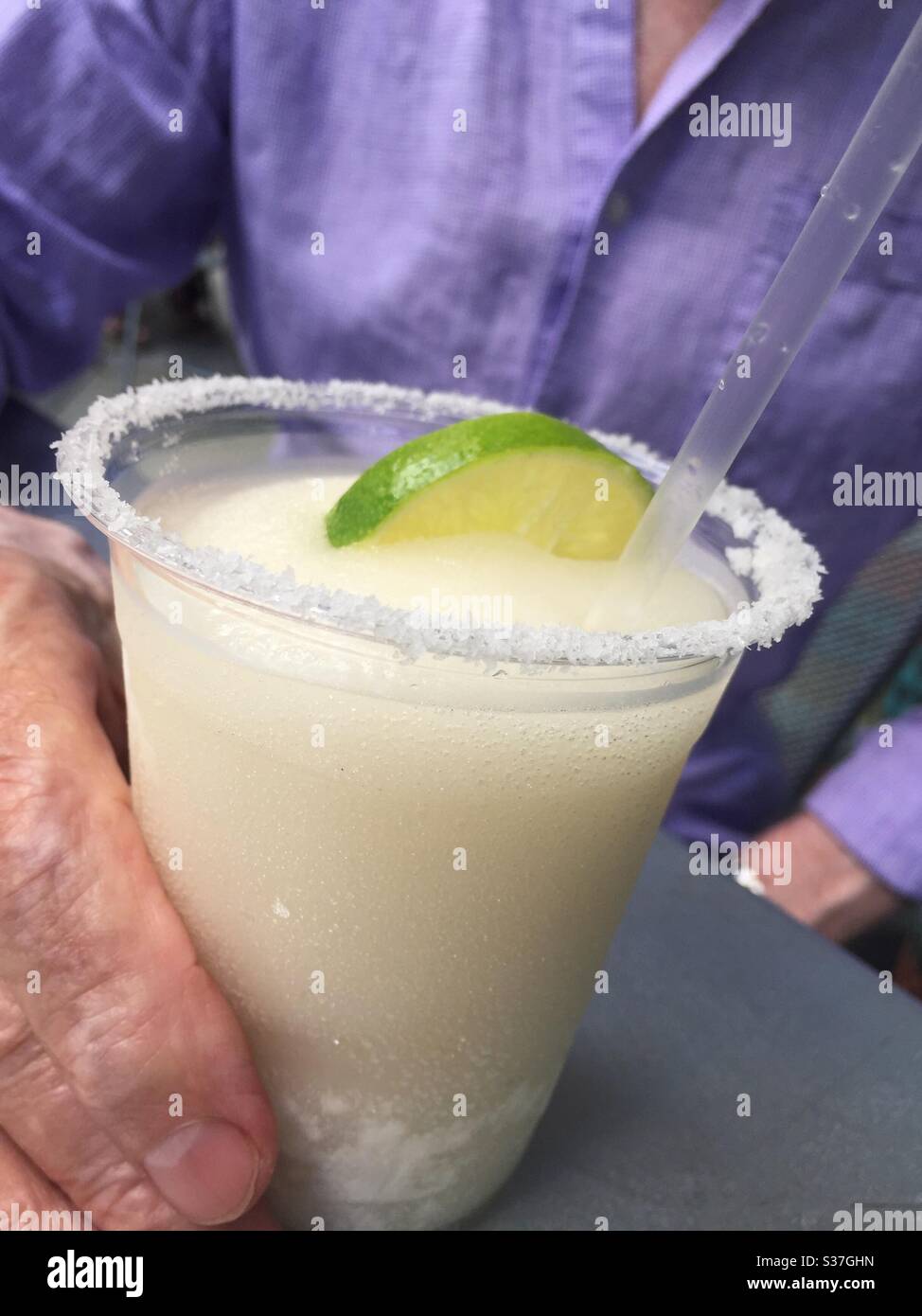 Caucasian man enjoying a refreshing frozen margarita in a plastic cup on a restaurant patio, USA - Smartphone Captured Stock Image