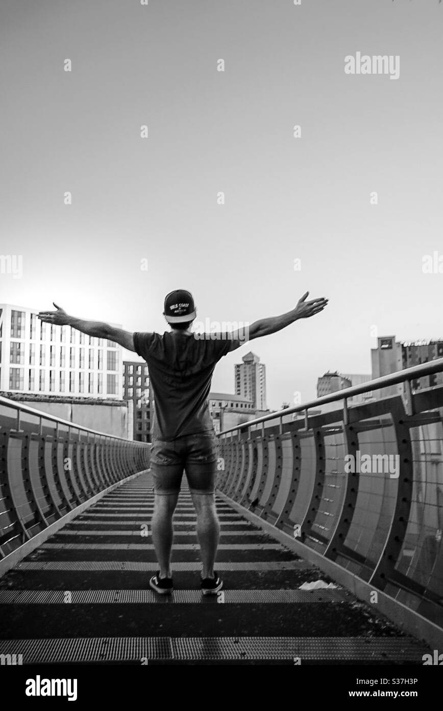 Man standing on bridge with arms wide. Stock Photo