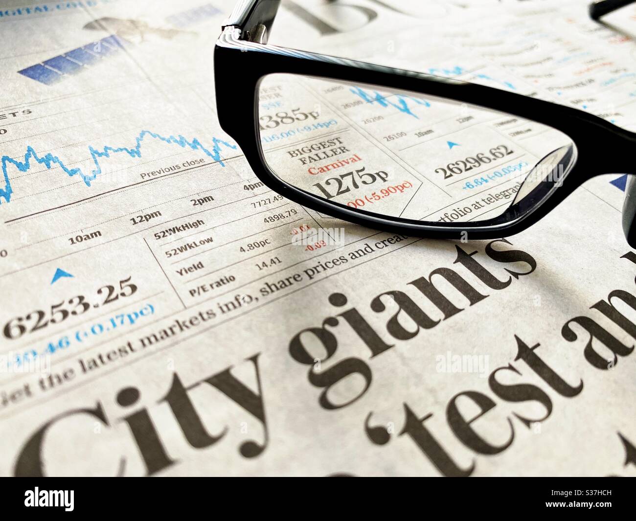 Business & finance concept. Closeup view of a financial newspaper with graph showing the FTSE 100 markets in a steady decline during the coronavirus crisis. Market crashing. With reading glasses - Smartphone Captured Stock Image
