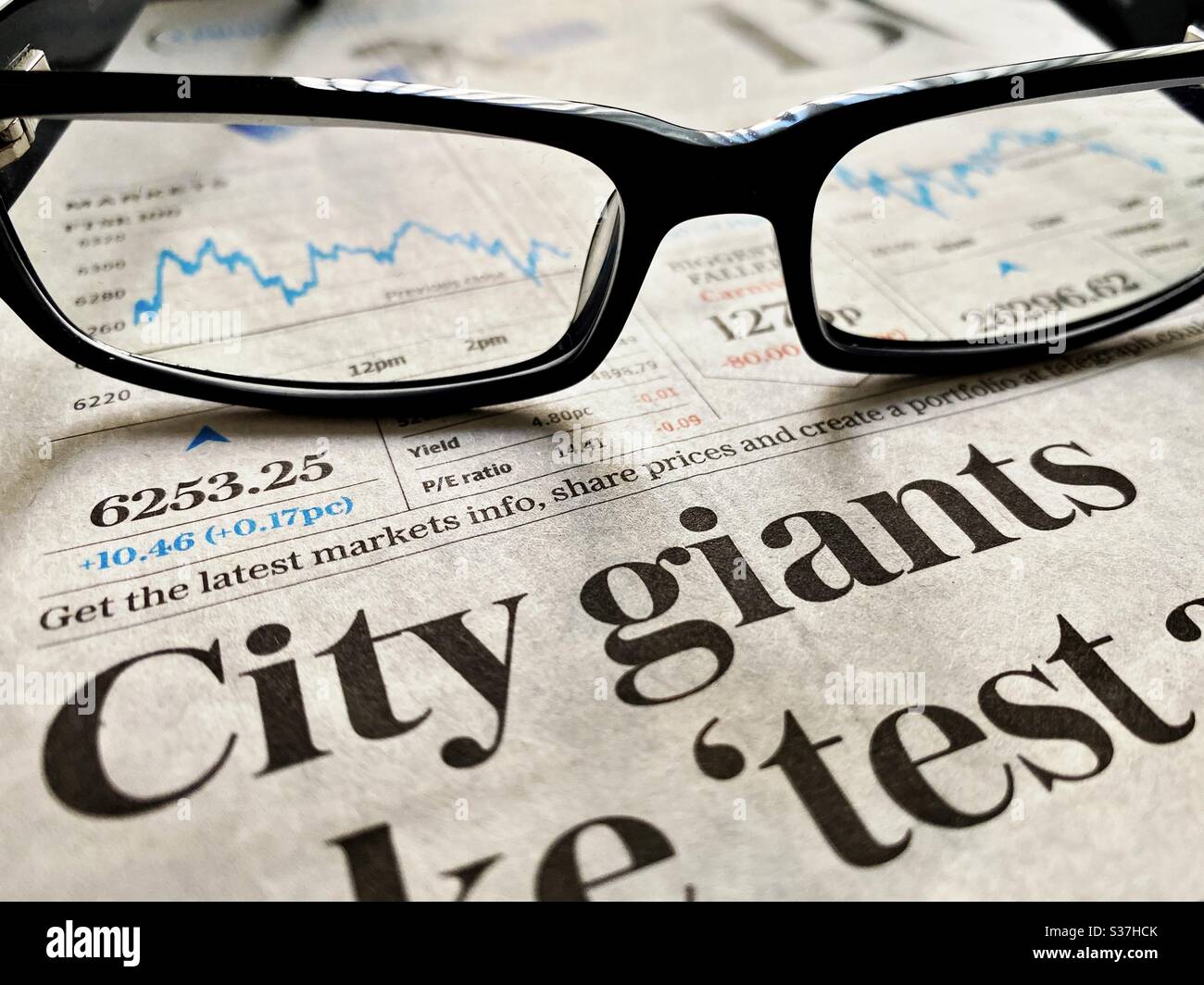 Business & finance concept. Closeup view of a financial newspaper with graph showing the FTSE 100 markets in a steady decline during the coronavirus crisis. Market crashing. With reading glasses - Smartphone Captured Stock Image