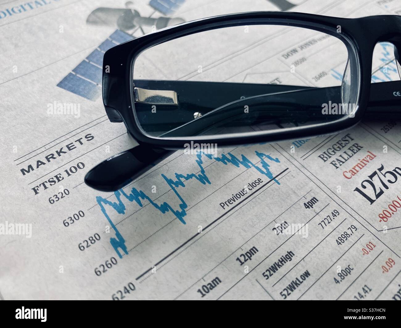 Business & finance concept. Closeup view of a financial newspaper with graph showing the FTSE 100 markets in a steady decline during the coronavirus crisis. Market crashing. With reading glasses - Smartphone Captured Stock Image