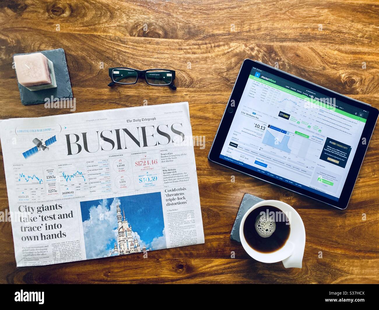 Business and finance concept. Closeup view market trader catching up on financial news with morning coffee, tablet device and business newspaper. FTSE 100 markets in  decline during coronavirus crisis - Smartphone Captured Stock Image