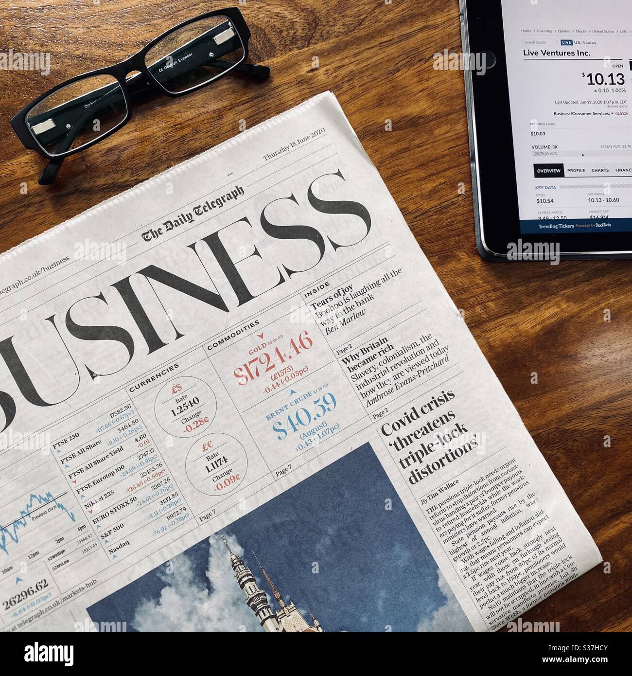 Business and finance concept. Closeup view market trader catching up on financial news with morning coffee, tablet device and business newspaper. FTSE 100 markets in  decline during coronavirus crisis - Smartphone Captured Stock Image