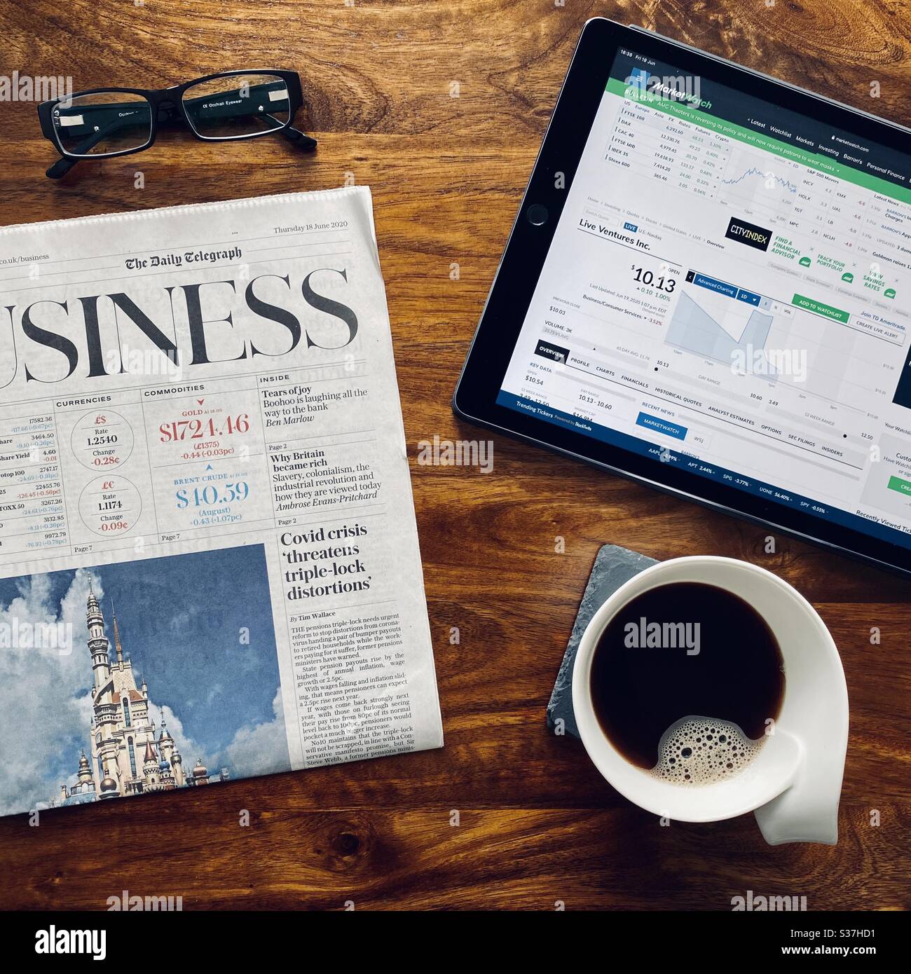 Business and finance concept. Closeup view market trader catching up on financial news with morning coffee, tablet device and business newspaper. FTSE 100 markets in decline during coronavirus crisis - Smartphone Captured Stock Image