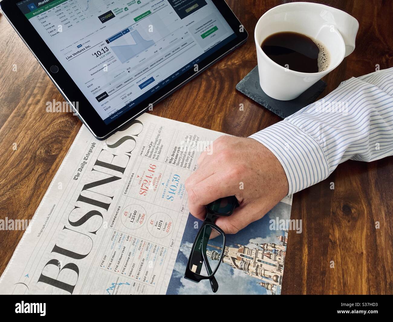 Business and finance concept. Closeup view market trader catching up on financial news with morning coffee, tablet device and business newspaper. FTSE 100 markets in decline during coronavirus crisis - Smartphone Captured Stock Image