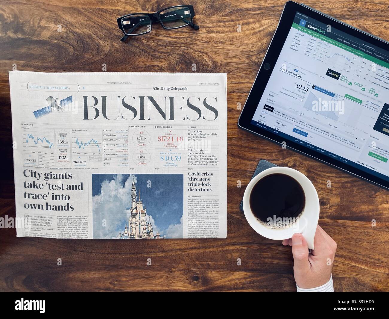 Business and finance concept. Closeup view market trader catching up on financial news with morning coffee, tablet device and business newspaper. FTSE 100 markets in decline during coronavirus crisis - Smartphone Captured Stock Image