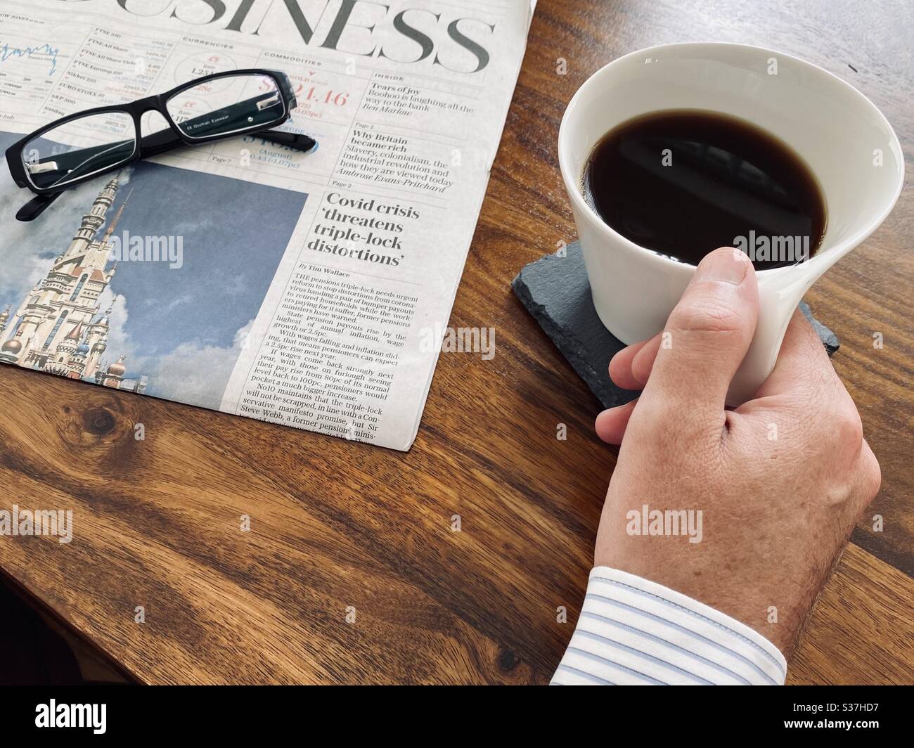 Business and finance concept. Closeup view market trader catching up on financial news with morning coffee, tablet device and business newspaper. FTSE 100 markets in decline during coronavirus crisis - Smartphone Captured Stock Image