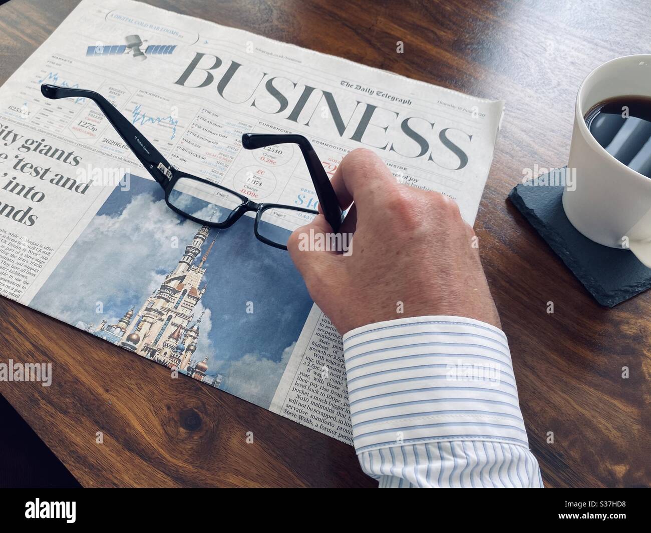 Business and finance concept. Closeup view market trader catching up on financial news with morning coffee, tablet device and business newspaper. FTSE 100 markets in decline during coronavirus crisis - Smartphone Captured Stock Image
