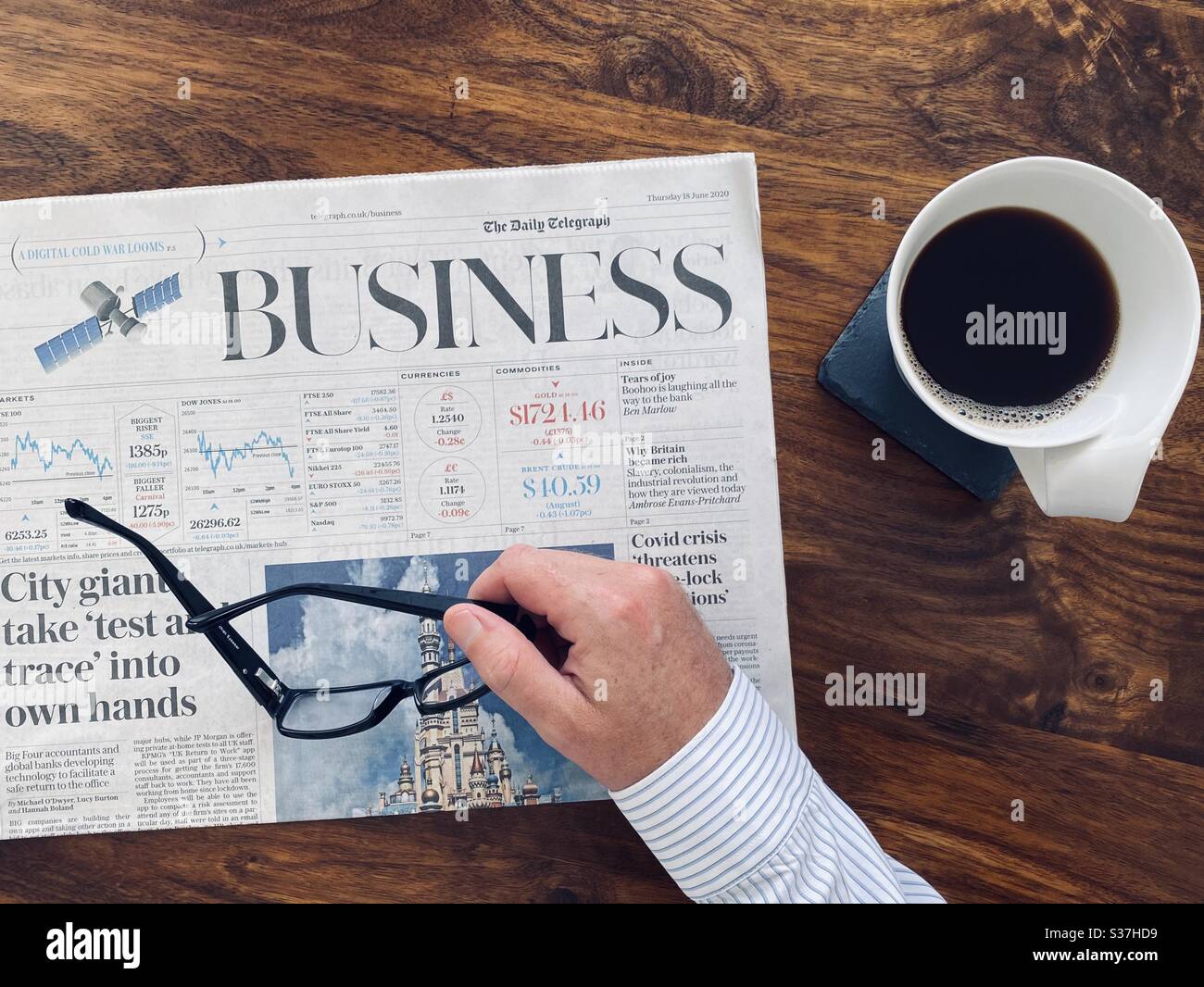 Business and finance concept. Closeup view market trader catching up on financial news with morning coffee, tablet device and business newspaper. FTSE 100 markets in decline during coronavirus crisis - Smartphone Captured Stock Image