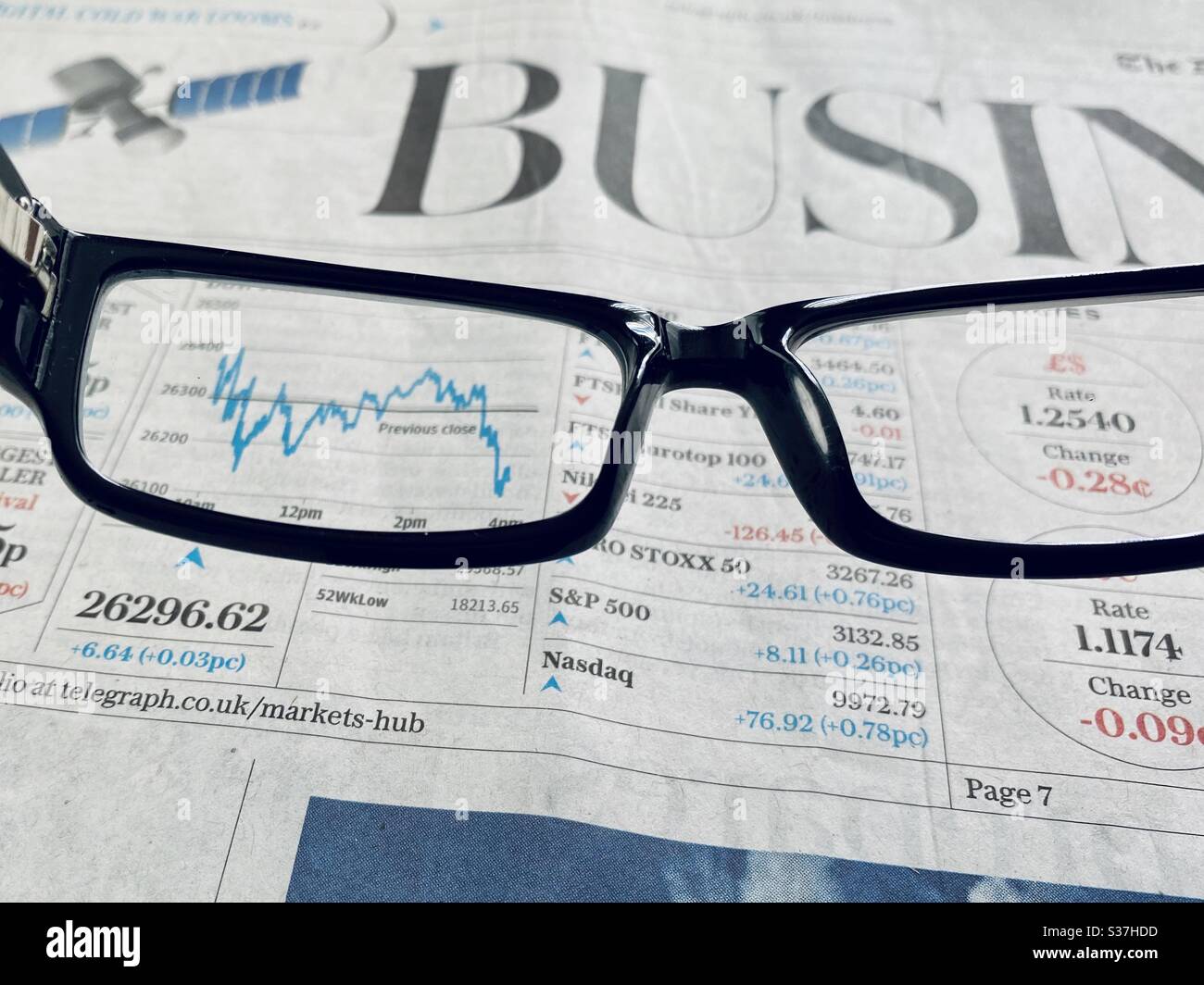 Business & finance concept. Closeup view of a financial newspaper with graph showing the FTSE 100 markets in a steady decline during the coronavirus crisis. Market crashing. With reading glasses - Smartphone Captured Stock Image