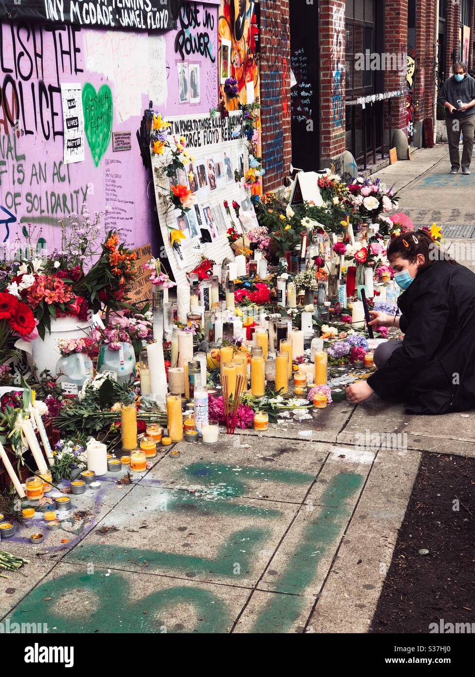 Woman wearing face mask lights candles at makeshift George Floyd memorial wall in CHOP CHAZ autonomous zone on Capitol Hill in Seattle, june 2020 Stock Photo