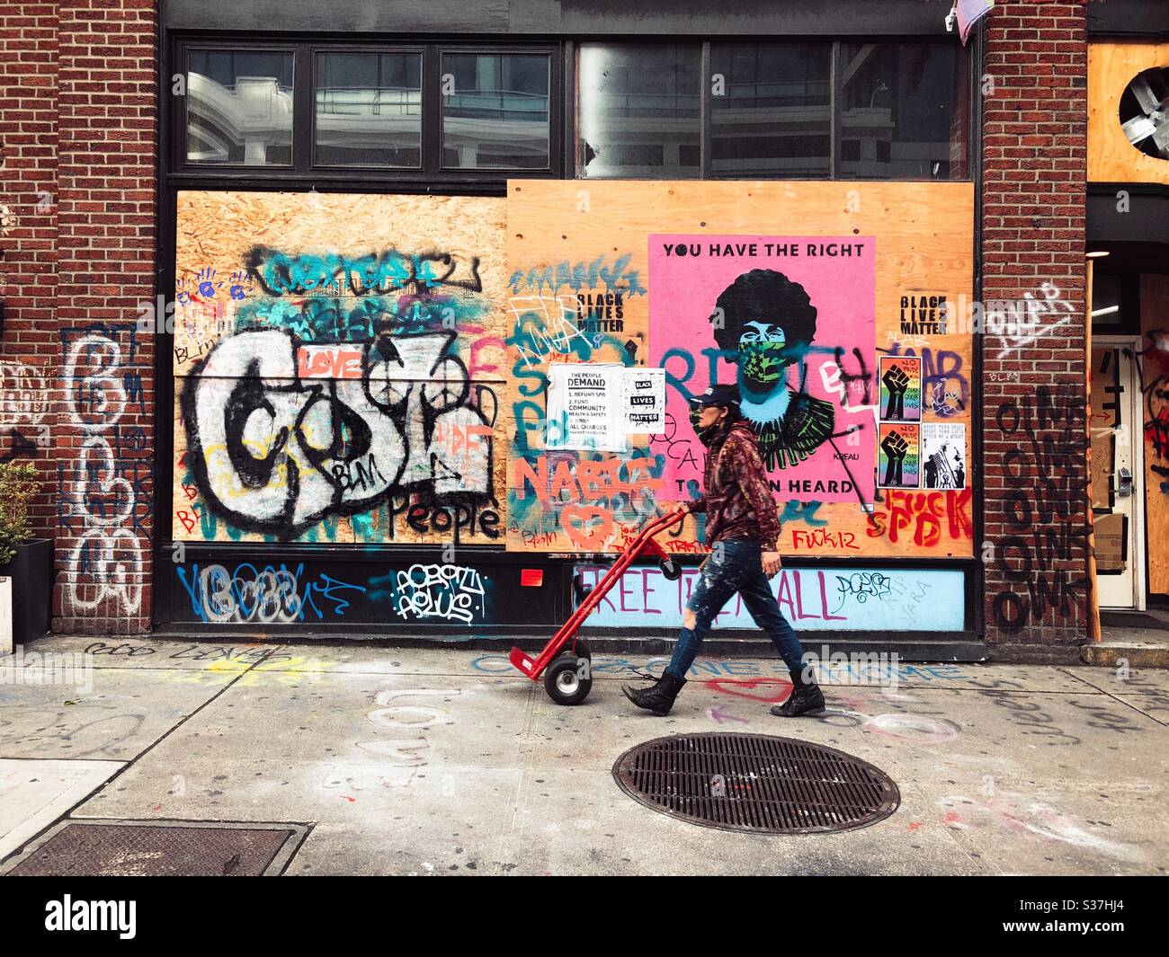 A person with heavy cart walking past mural and graffiti on the wall of a building in CHAZ CHOP autonomous zone on Capitol Hill in Seattle, June 2020 - Smartphone Captured Stock Image