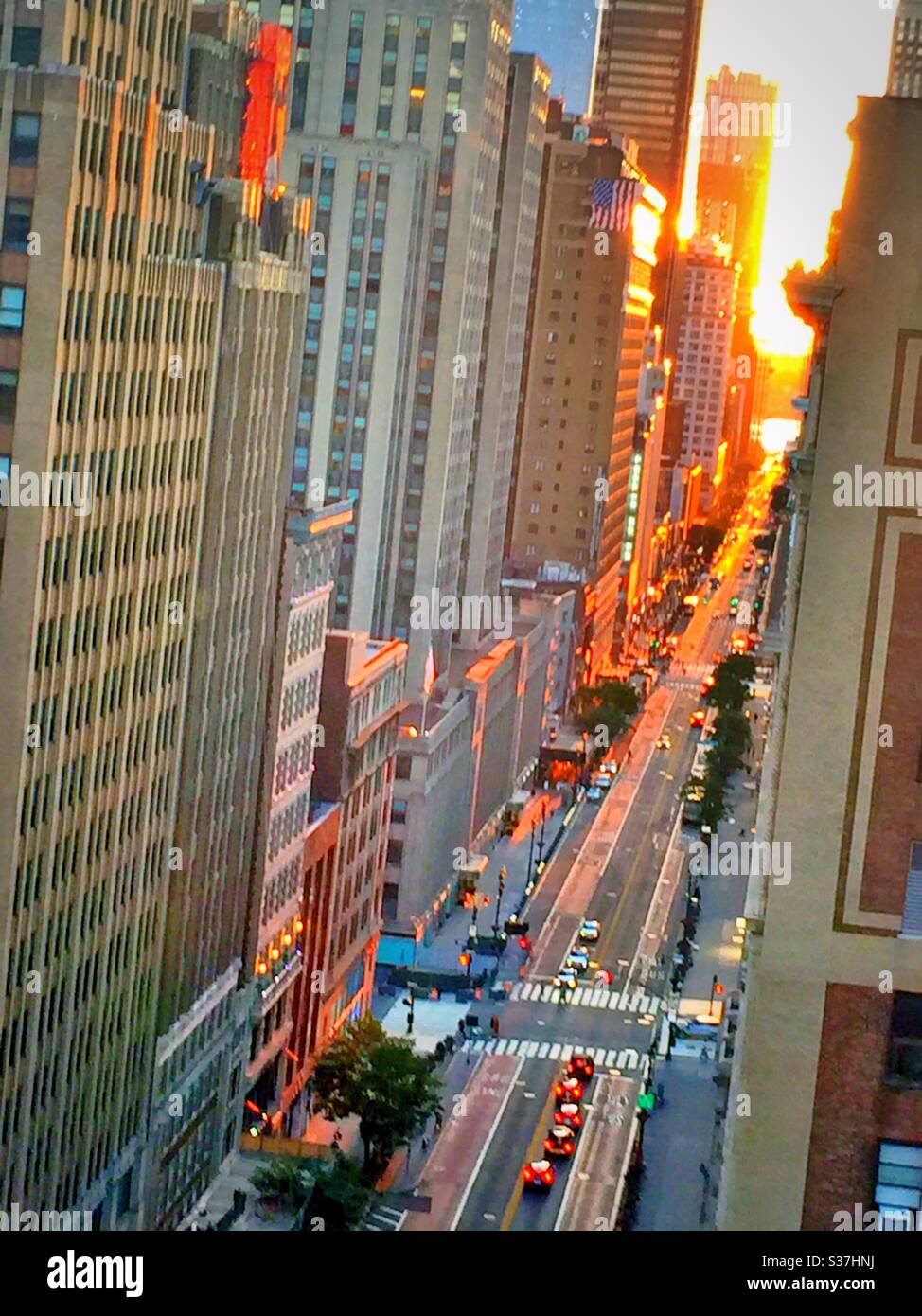 The setting sun casts a golden glow down 34th St. during  Manhattanhenge in June of each year, NYC, USA - Smartphone Captured Stock Image