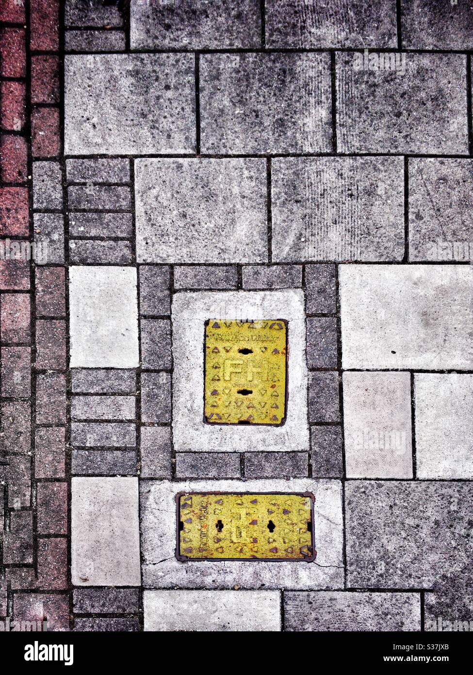 Two painted metal panels a pavement. The yellow stands out boldly against the greys and faded pinks of the paving stones and bricks. Fascinating pattern of squares and rectangles. Beautiful grunge. Stock Photo