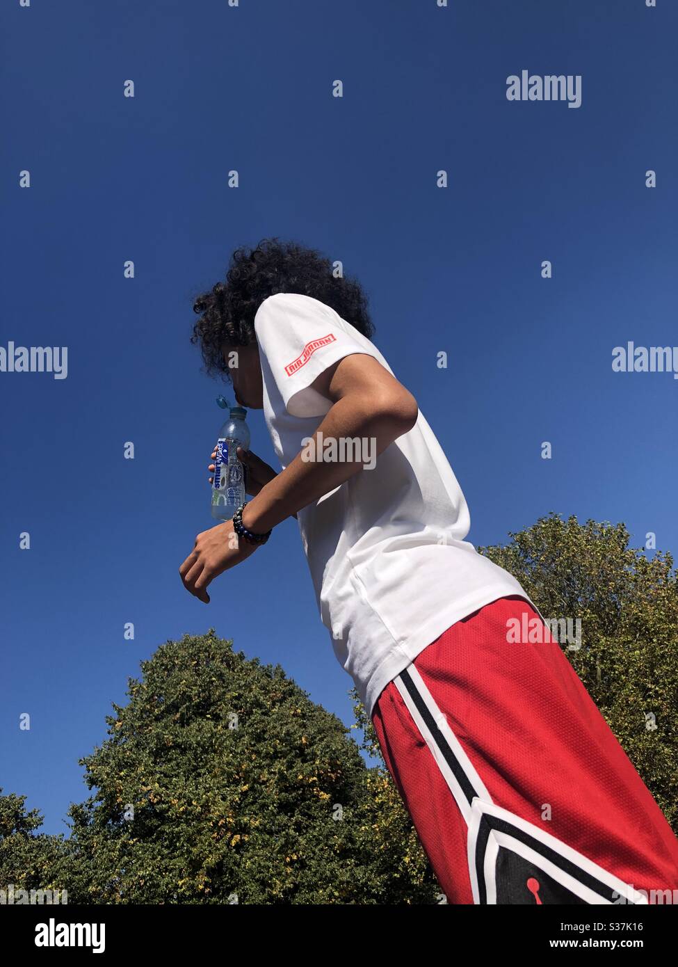Young guy drinking a bottle of water after playing basketball on a hot summers day - Smartphone Captured Stock Image
