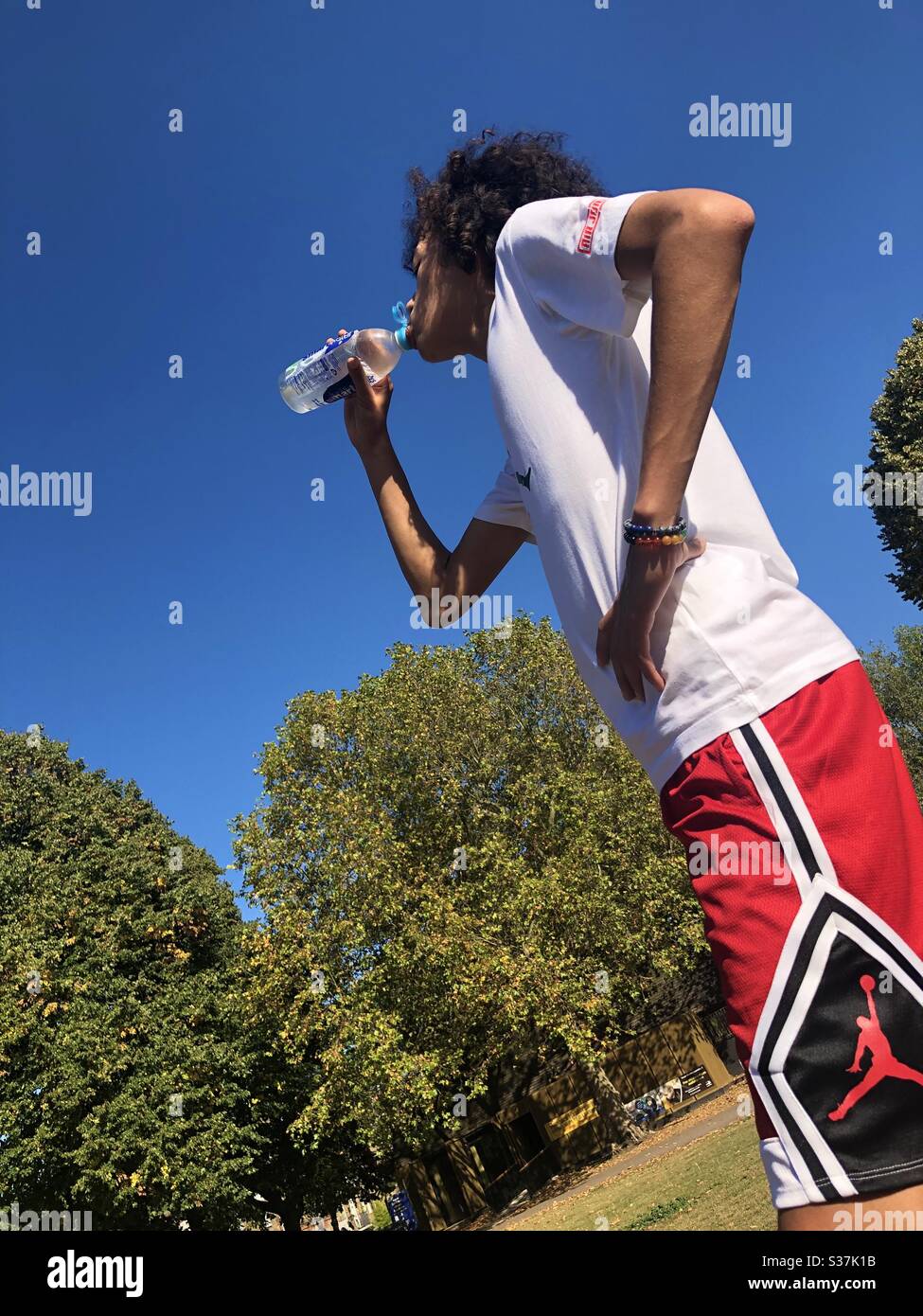 Young guy drinking a bottle of water after playing basketball on a hot summer day - Smartphone Captured Stock Image