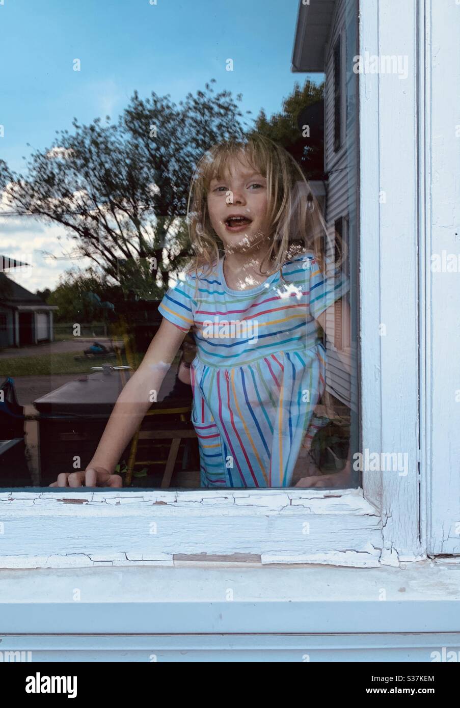 Girl at a window with outside reflected on glass. - Smartphone Captured Stock Image