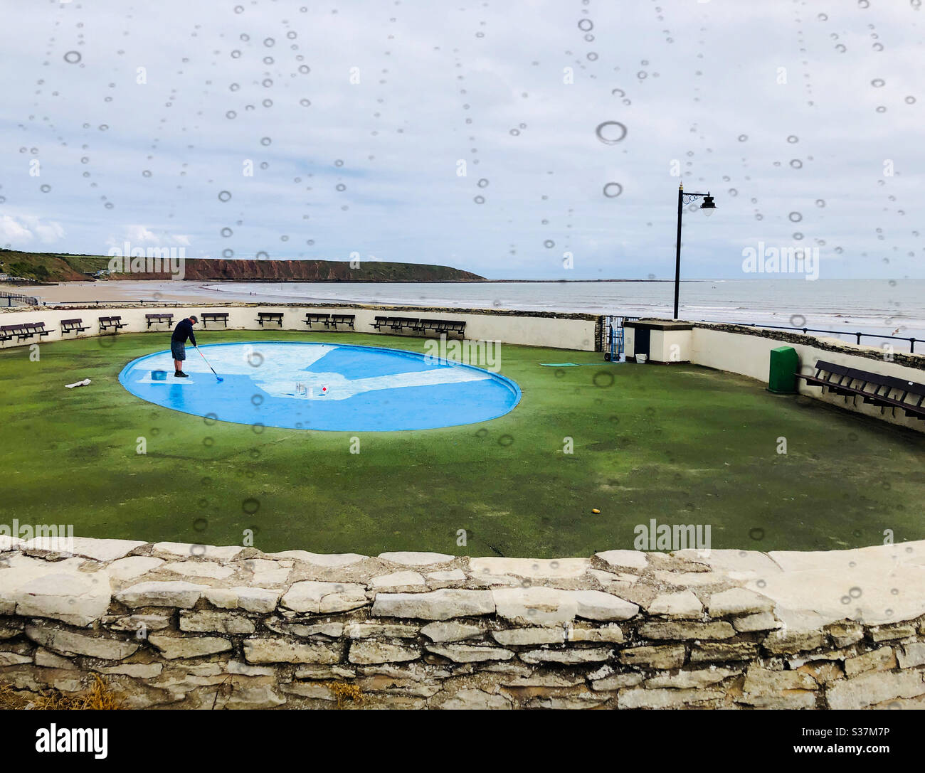 Man repainting the base of a shallow paddling pool - Smartphone Captured Stock Image