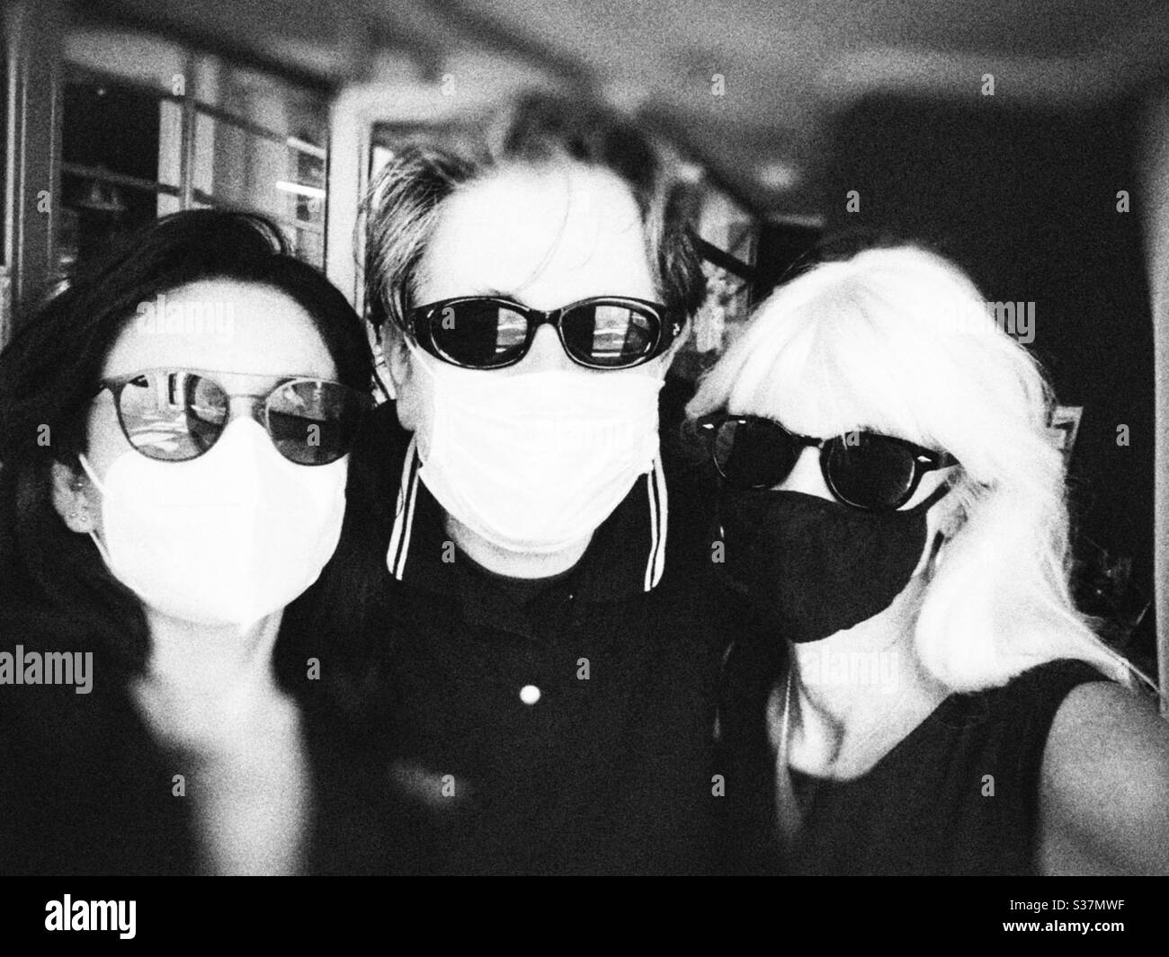 Latina woman , european man and blond lady in black and white wearing surgical face mask and sunglasses in summer time. - Smartphone Captured Stock Image