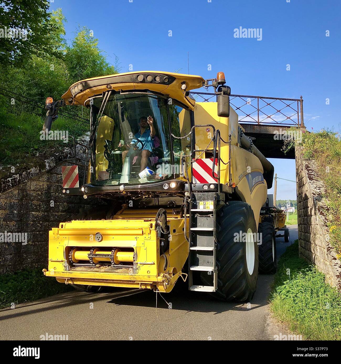 New Holland combine harvester squeezing under a low railway bridge - sud-Touraine, France. Stock Photo