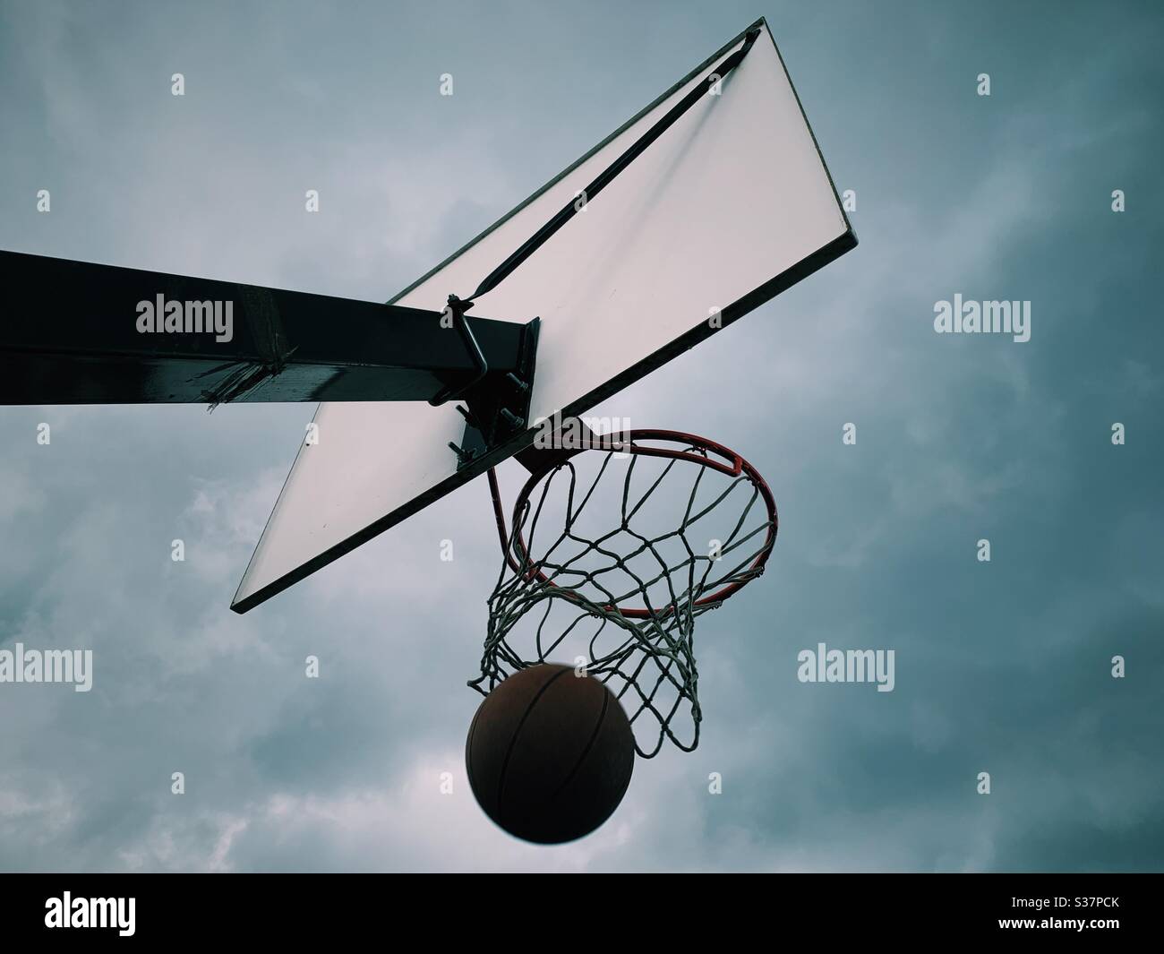 A basket ball lands through a hoop with a dramatic sky - Smartphone Captured Stock Image
