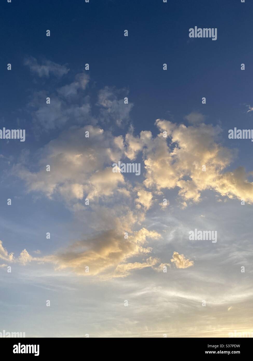 Sun lighting up white swirling clouds with blue skies Stock Photo