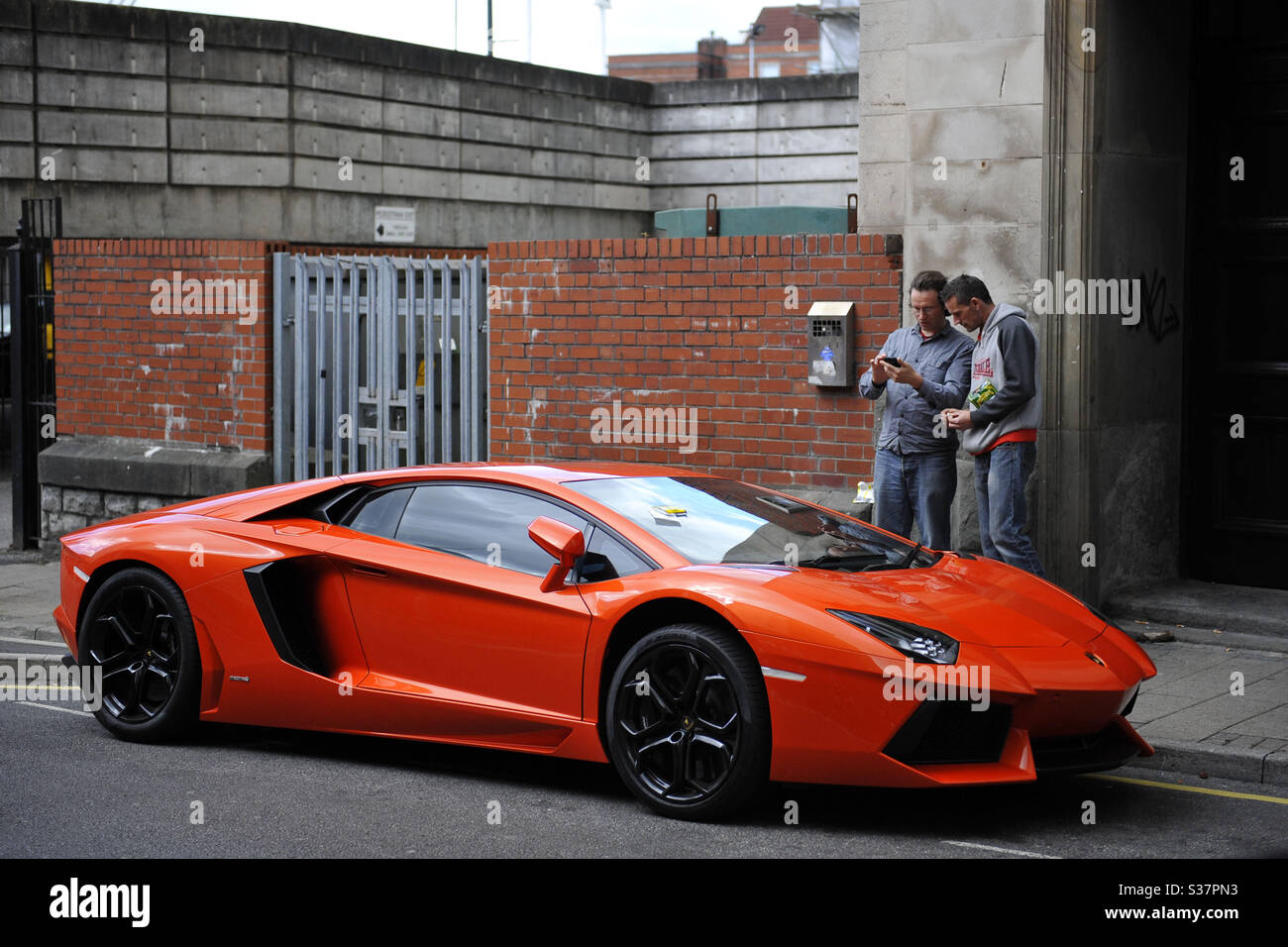 Two men look at an orange Lamborghini Aventador parked in central Cardiff,  Wales, UK, where it was given a parking ticket Stock Photo - Alamy