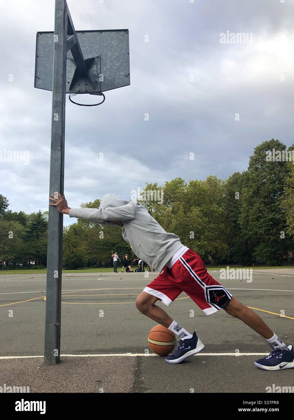Young guy warming up to play basketball on a court in London - Smartphone Captured Stock Image
