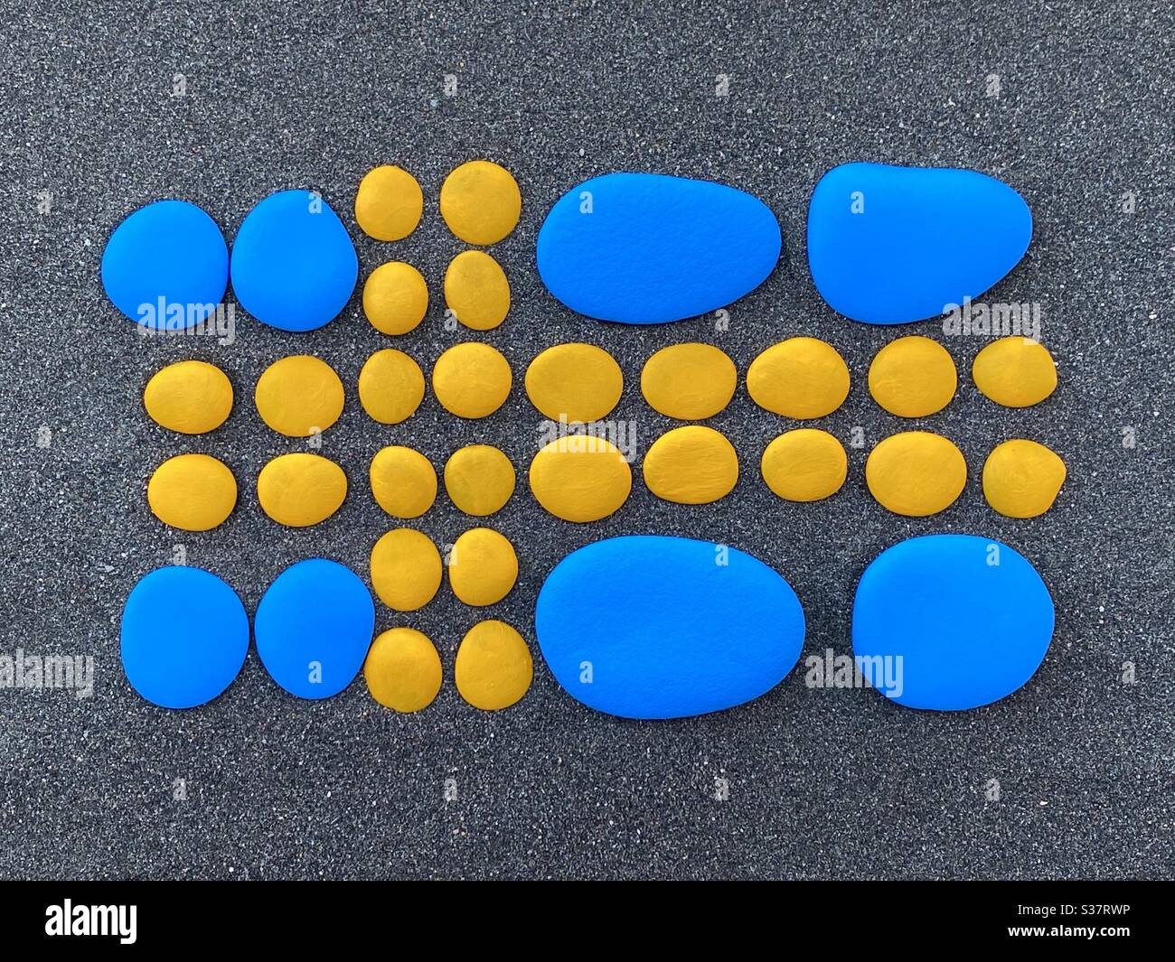 Swedish flag composed with yellow and blue painted pebbles over black volcanic sand - Smartphone Captured Stock Image