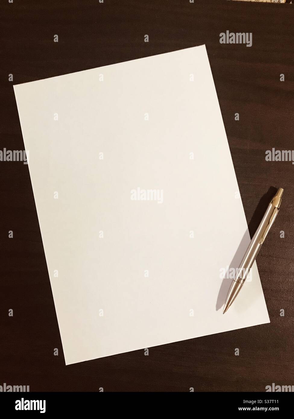 Blank empty paper sheet with a silver coloured pen beside on laminated  background - empty page ,copy space for your own text “words are unlimited, use it wisely” my own quote in a dramatic look Stock Photo