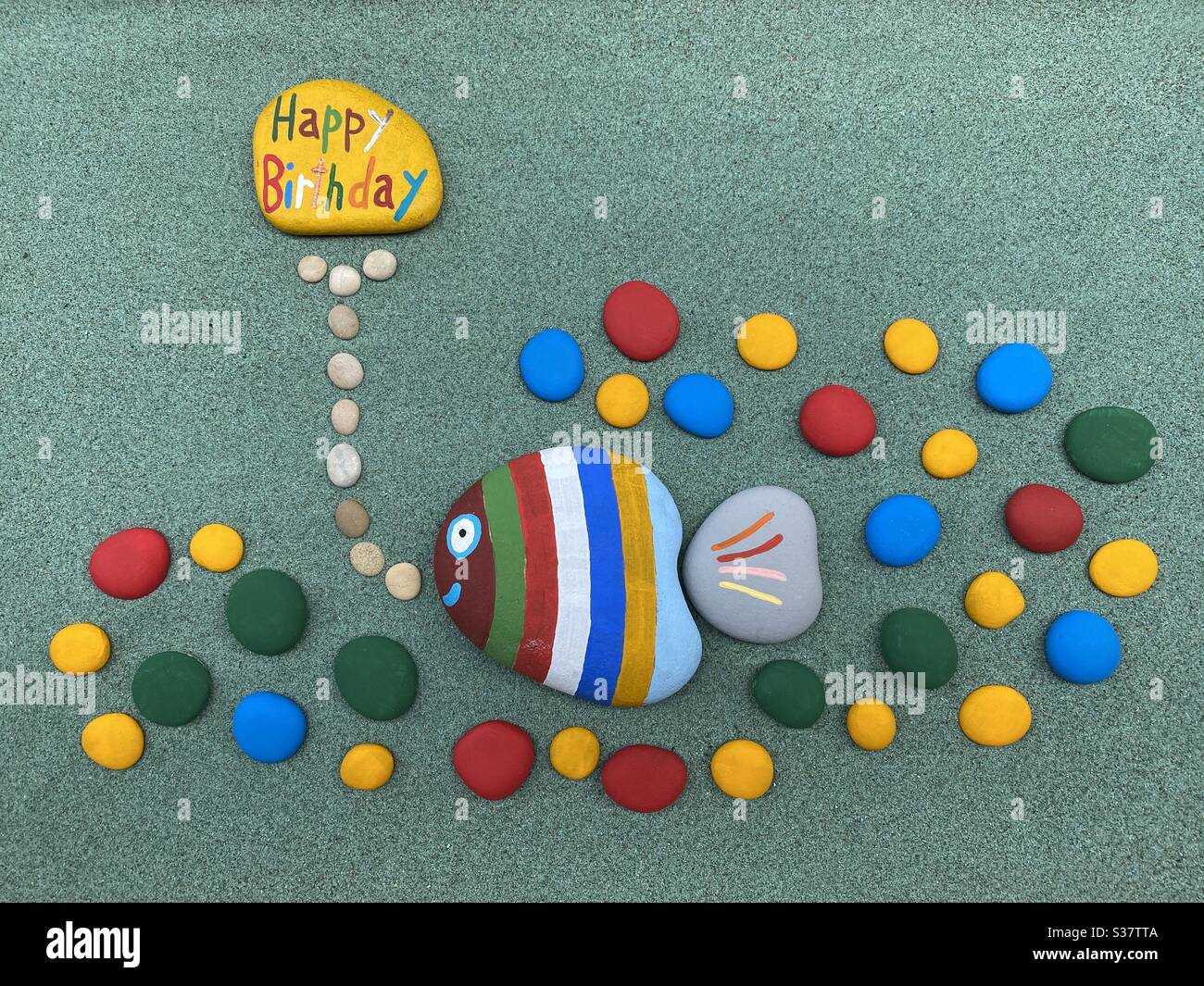 Happy Birthday composition with funny colorful stones over green sand Stock Photo