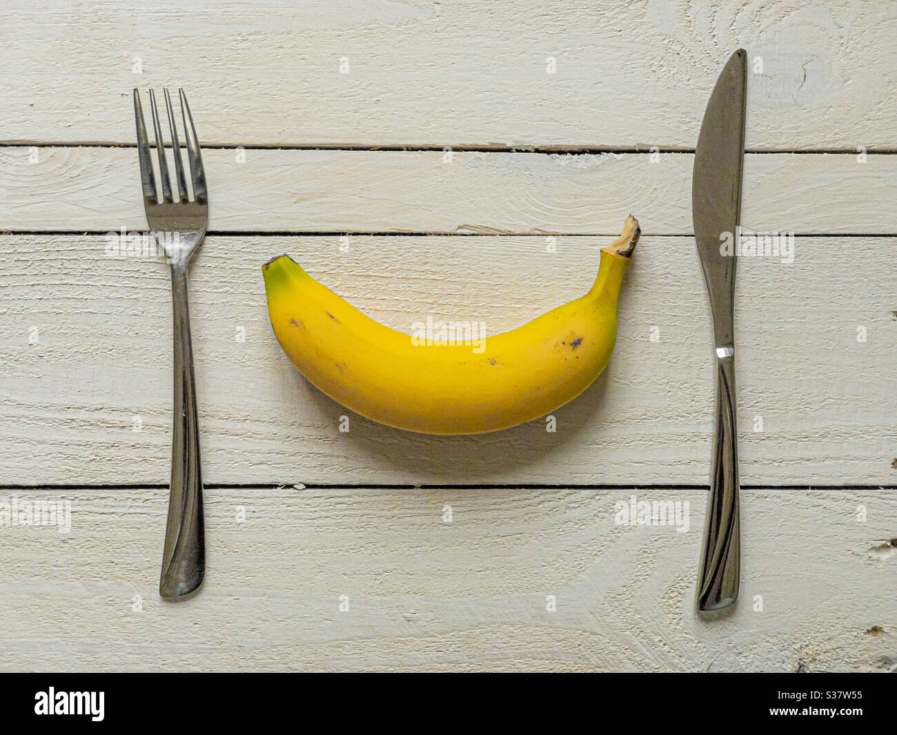 Yellow banana with knife and fork on white wooden planks - Smartphone Captured Stock Image