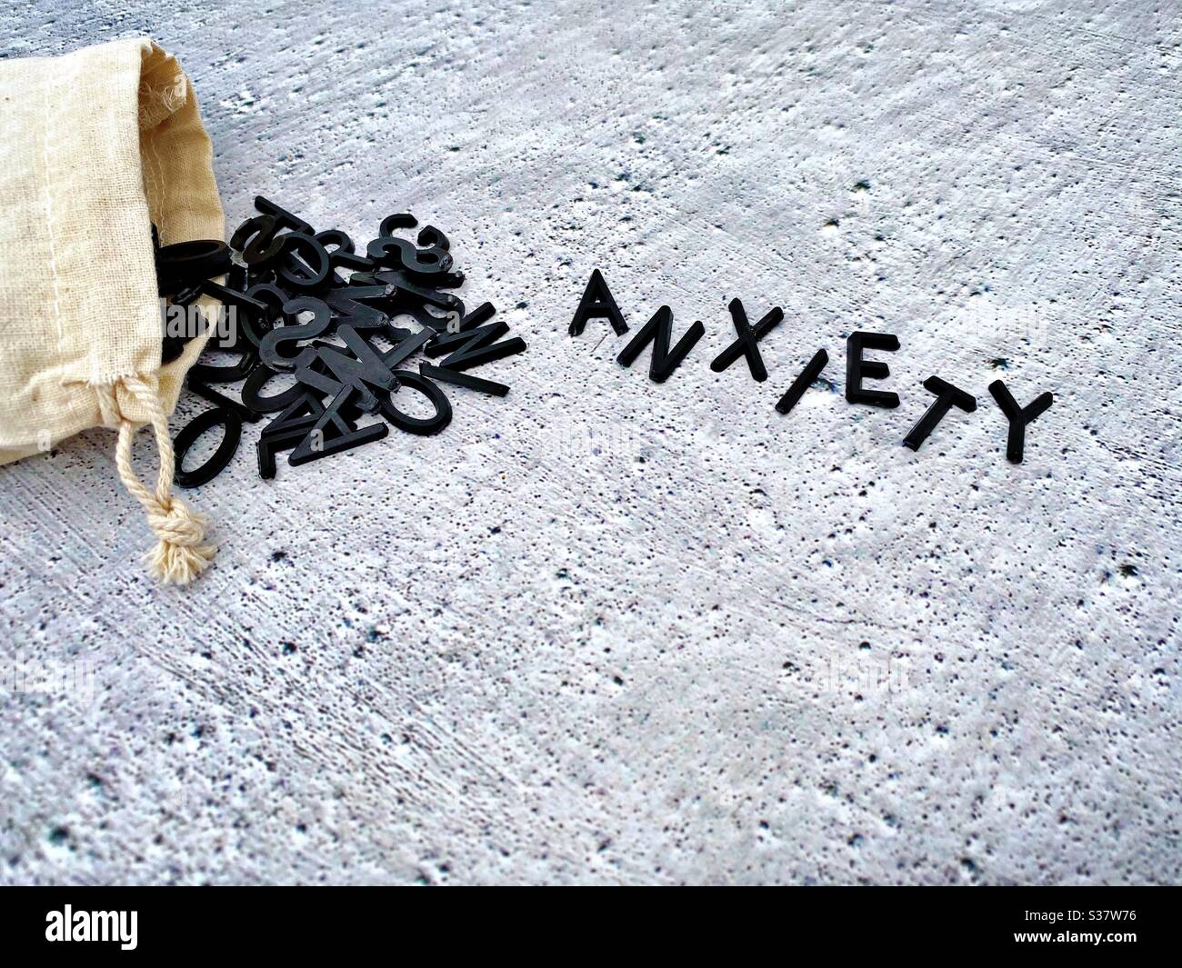 Closeup view of black letters spilling out of a small hessian bag. Spelling the word anxiety. Against a cold rough textured concrete background. Mental health awareness. - Smartphone Captured Stock Image