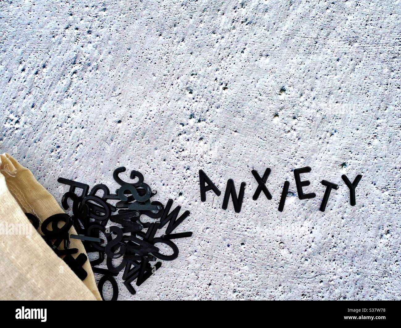 Closeup view of black letters spilling out of a small hessian bag. Spelling the word anxiety. Against a cold rough textured concrete background. Mental health awareness. - Smartphone Captured Stock Image