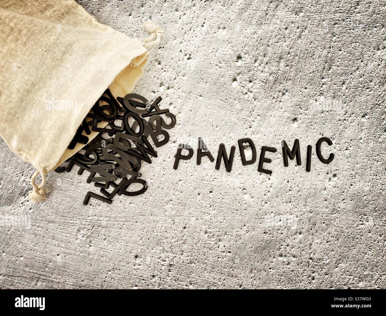 Black letters spilling out of a small hessian bag spelling the word Pandemic. Against a textured concrete background. Stock Photo