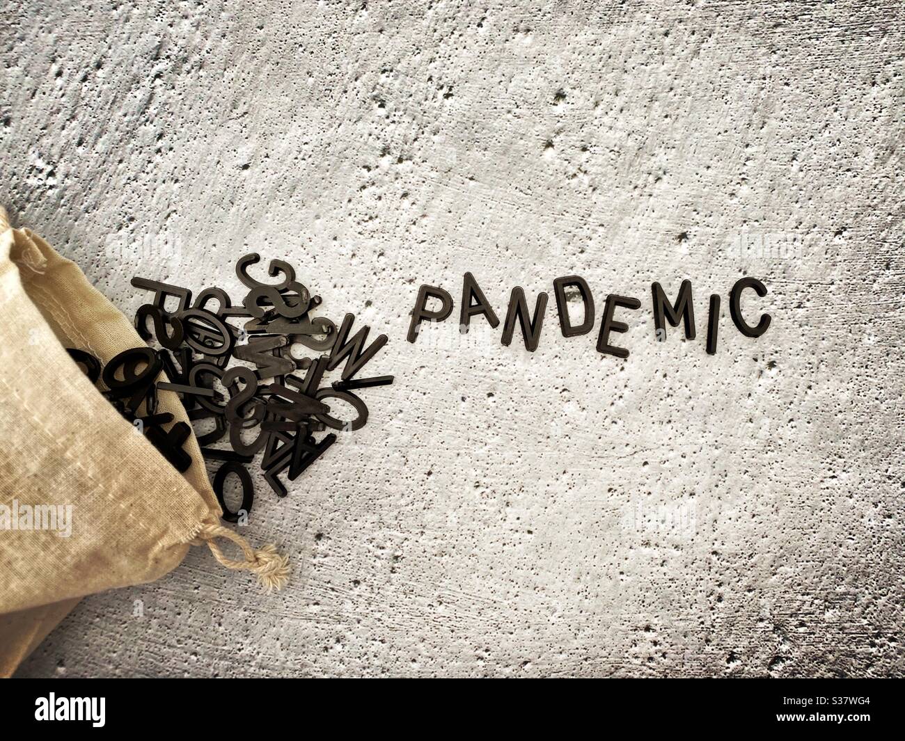 Black letters spilling out of a small hessian bag spelling the word Pandemic. Against a textured concrete background. - Smartphone Captured Stock Image