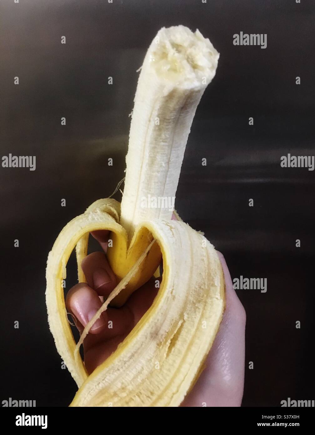 Hand holding partially peeled banana with a bite out of it - Smartphone Captured Stock Image