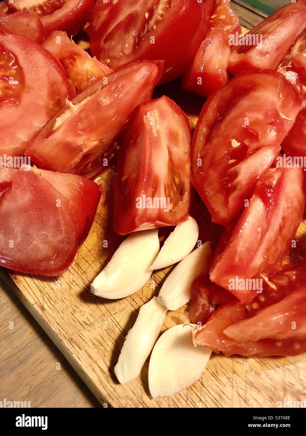 Chopped tomatoes and garlic cloves on chopping board. - Smartphone Captured Stock Image
