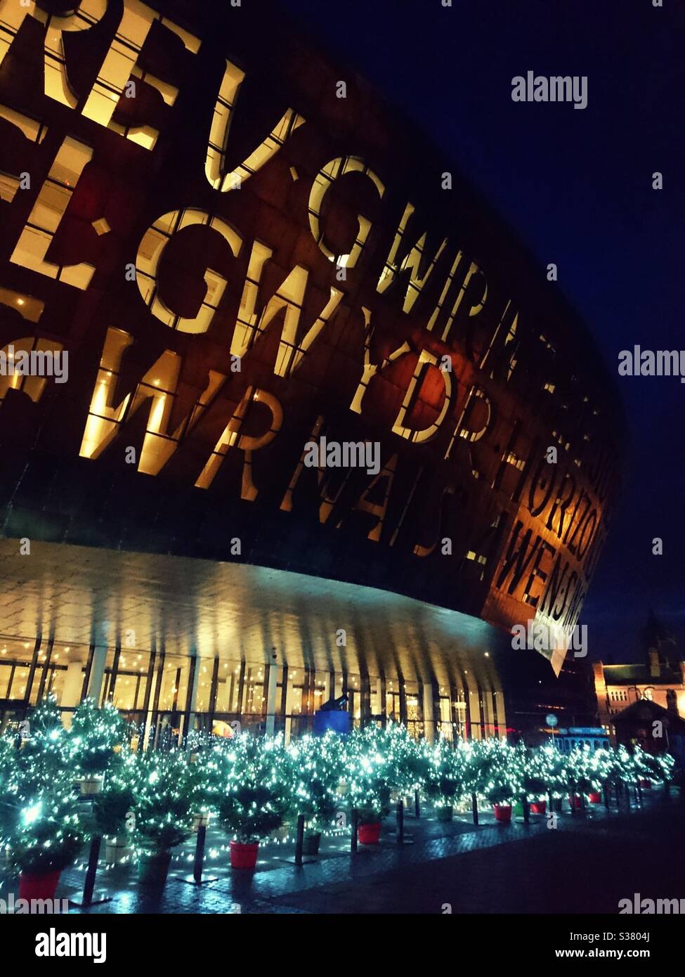 A photograph of the Wales Millennium Centre in Cardiff Bay at Christmastime. Christmas trees arranged outside. Festive feel. - Smartphone Captured Stock Image