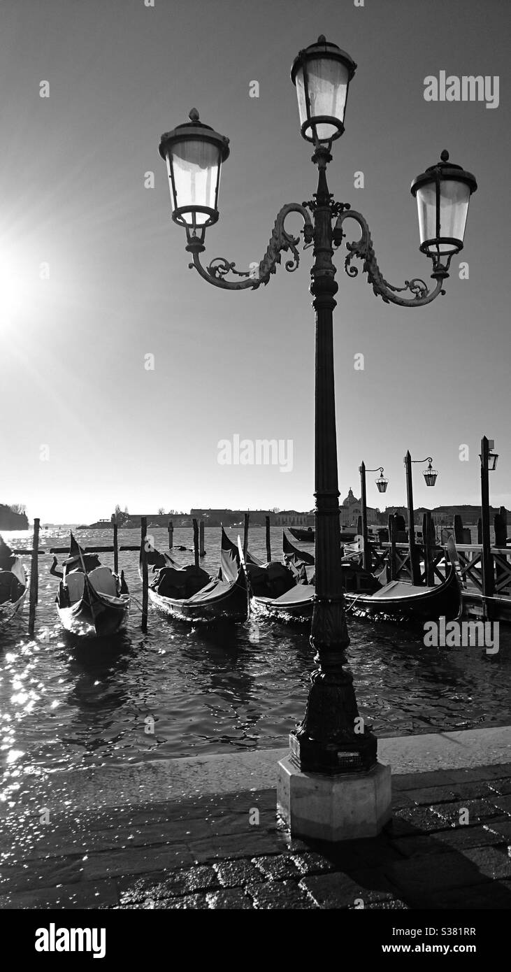 A black and white photograph of a traditional style streetlamp and gondolas in Venice on a sunny day. European tourism destination - Smartphone Captured Stock Image