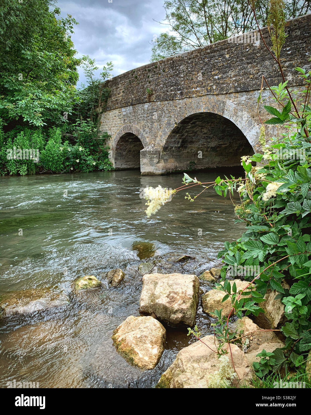 Water running underneath a bridge. The River Windrush near the village of Asthall, Oxfordshire in the Cotswolds. Stock Photo