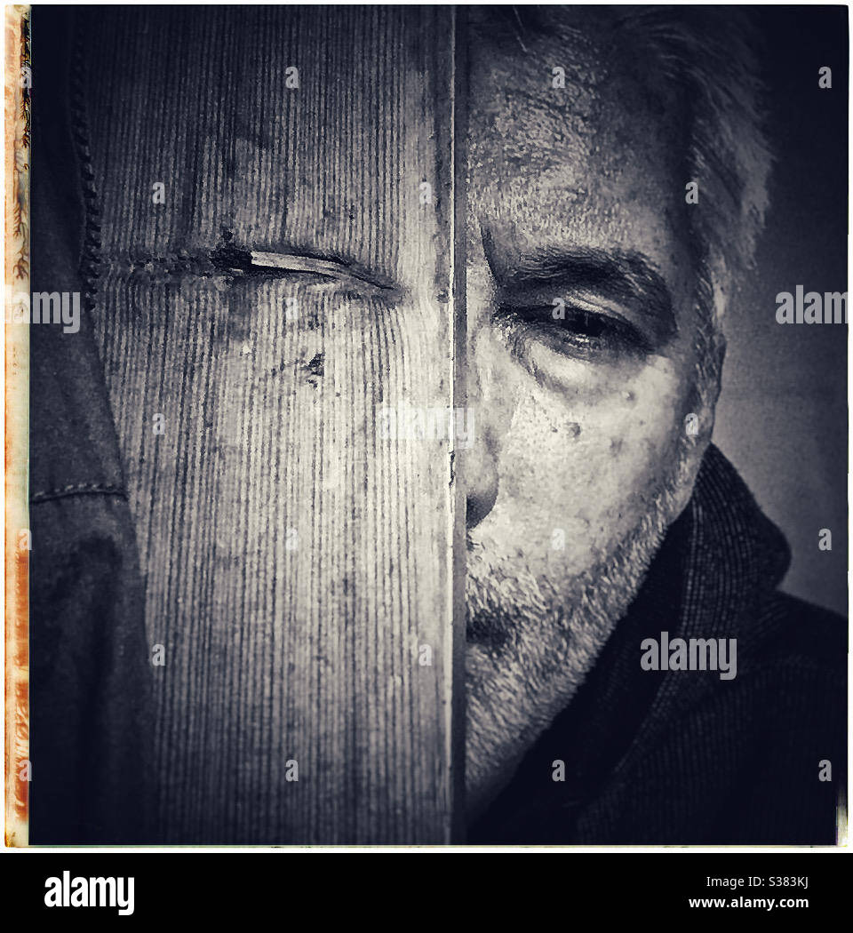 A weathered face peeks out from behind a wooden door - Smartphone Captured Stock Image