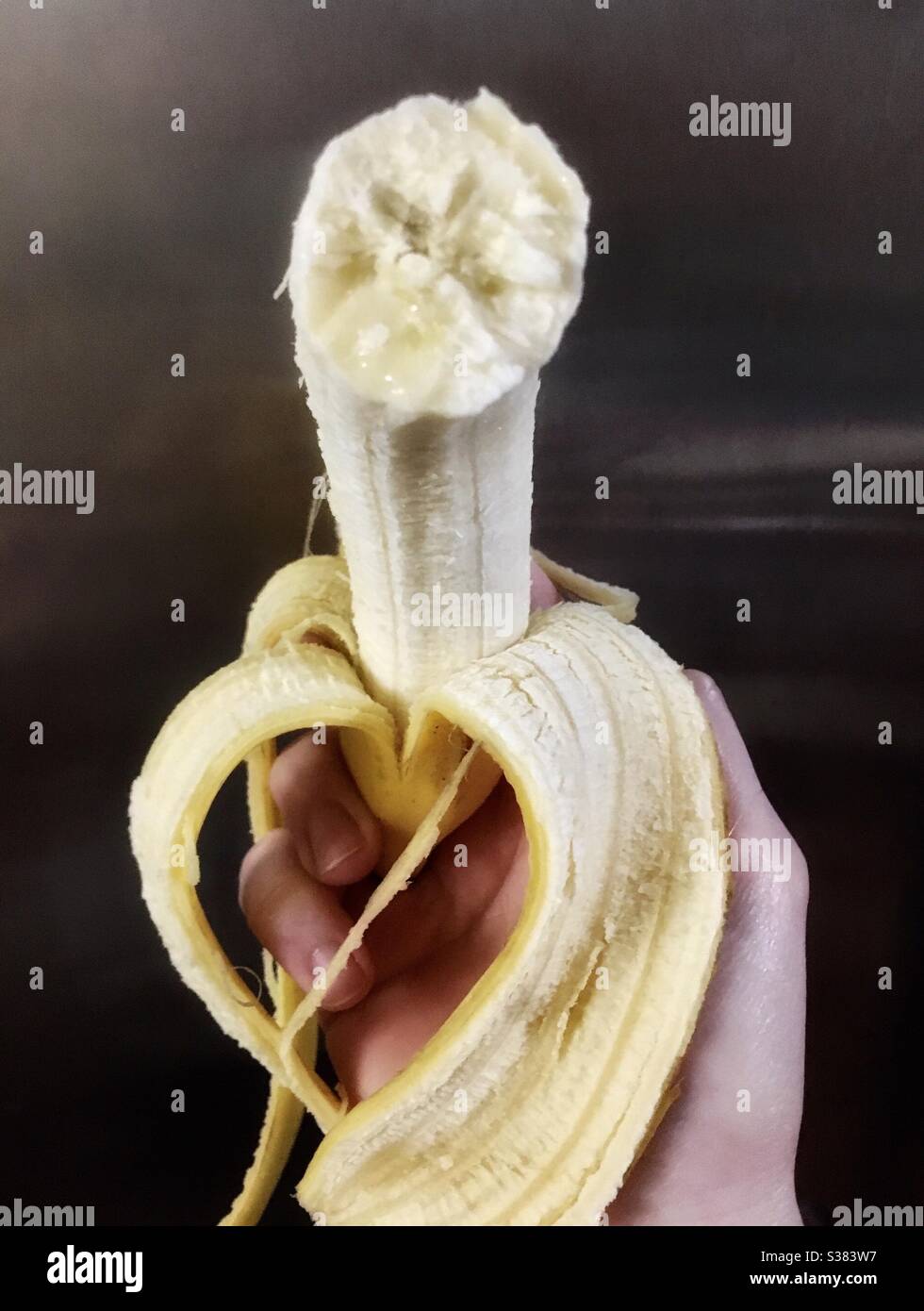 Hand holding partially peeled banana with a bite out of it Stock Photo