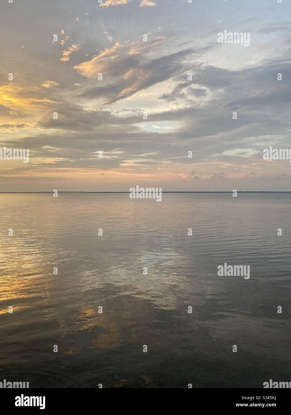 Colorful sunset skies with layers of clouds reflecting onto still bay ...