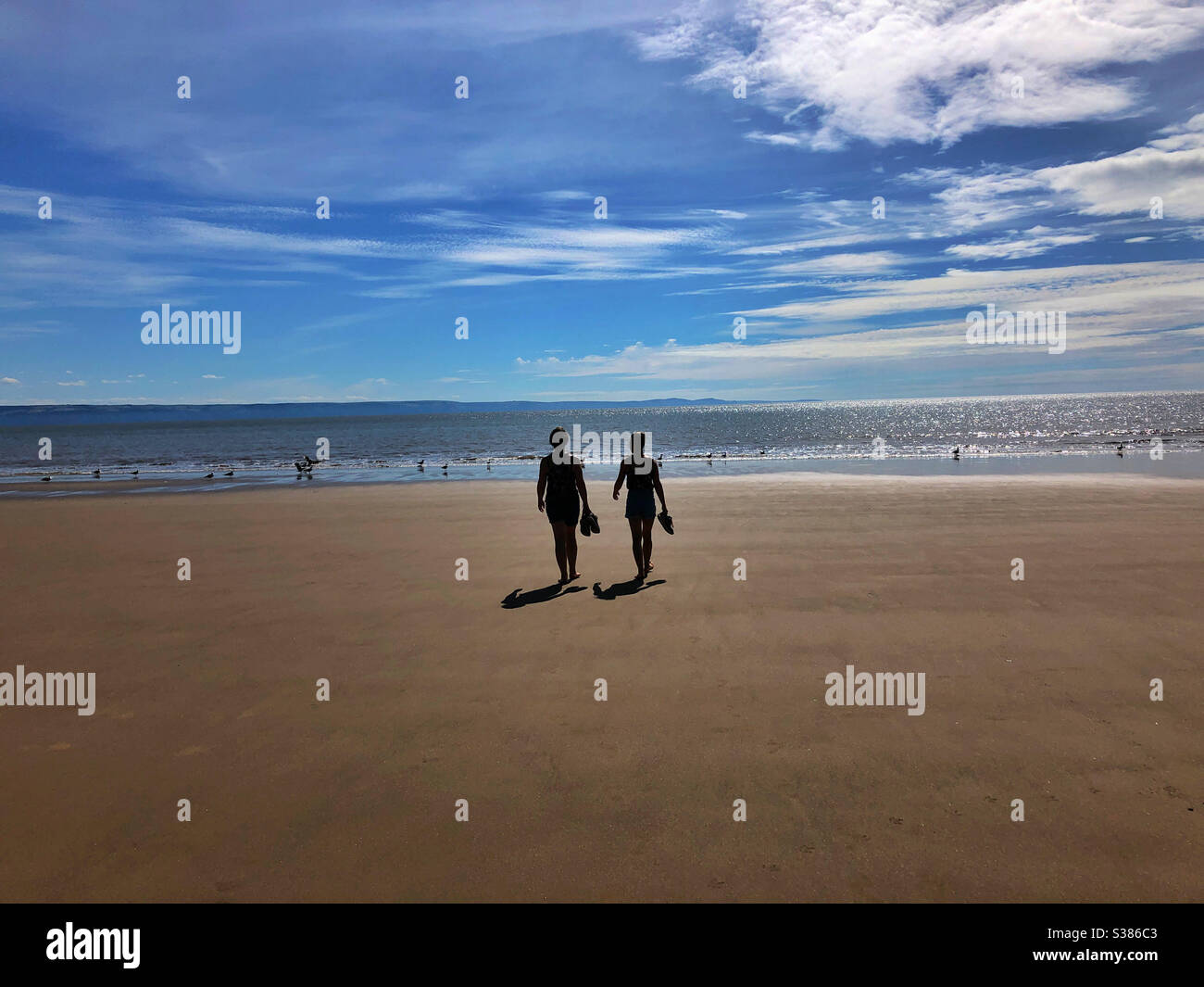 Mother and daughter walking towards the sea for a paddle with their shoes in their hands. - Smartphone Captured Stock Image