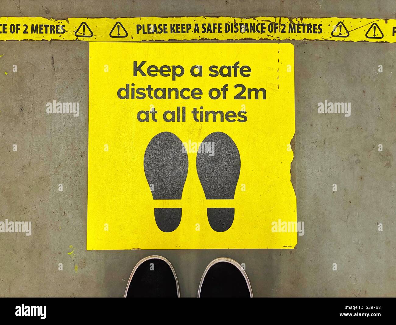 Two feet alongside a sign on the floor of a store instructing shoppers to maintain social distancing. - Smartphone Captured Stock Image